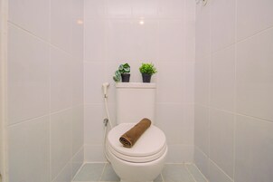 A bathroom with a white toilet, a towel on the seat, and two potted plants on the tank.