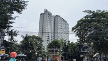 A tall residential building with multiple floors and balconies, surrounded by trees and power lines.