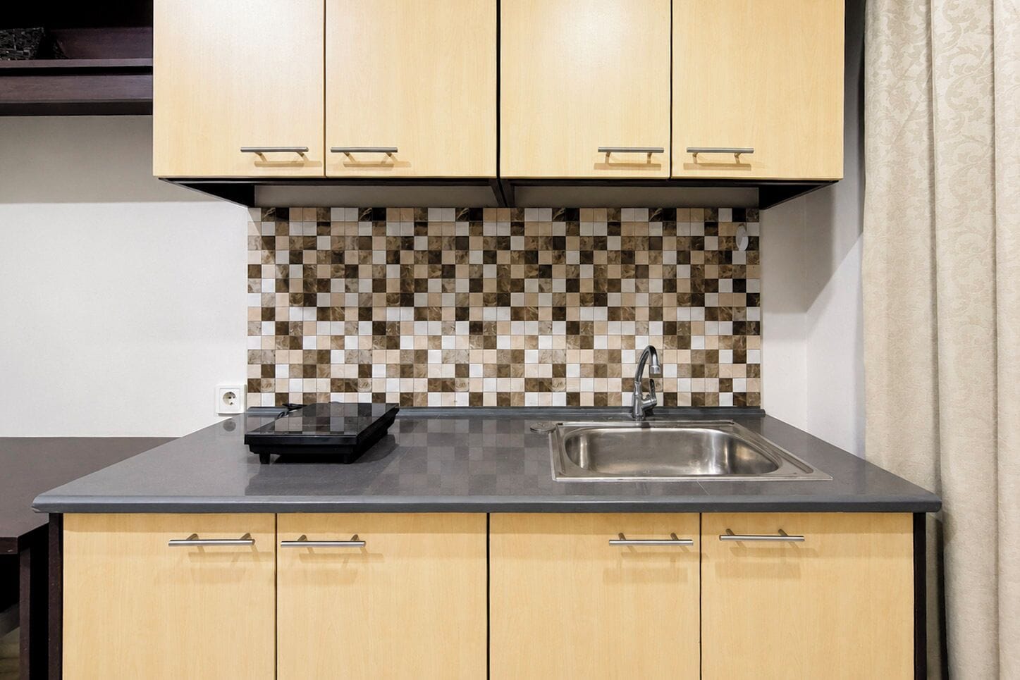 A kitchen with wooden cabinets, a tiled backsplash, and a stainless steel sink.