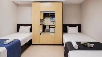 A hotel room with two beds, a wardrobe, a desk, and a small kitchenette.