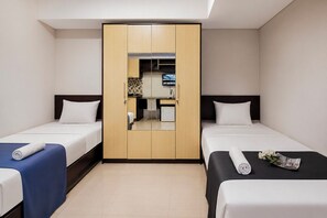 Quarto de hotel com duas camas, um guarda-roupa, uma escrivaninha e uma pequena cozinha.