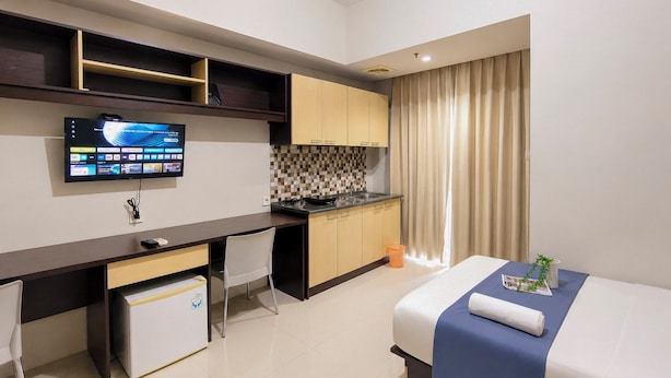 A modern hotel room with a bed, a desk, a kitchenette, and a television. - Urban Cozy Studio At Apartment Skyland City Jatinangor (Sumedang)