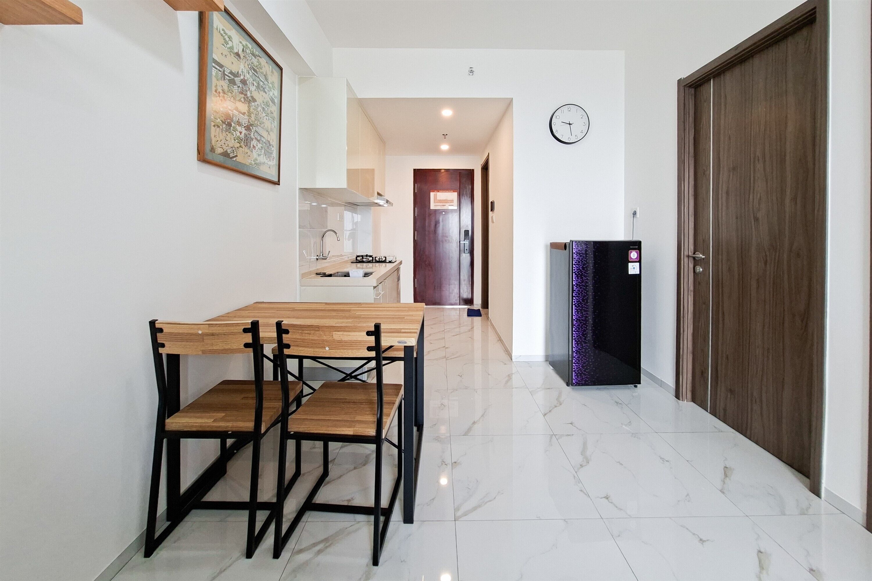 Un pasillo con una mesa de comedor y sillas, un reloj en la pared y una puerta a la derecha.
