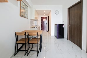 A hallway with a dining table and chairs, a clock on the wall, and a door on the right. - Beautifully Designed 2Br At Apartment Sky House Bsd (Pagedangan)