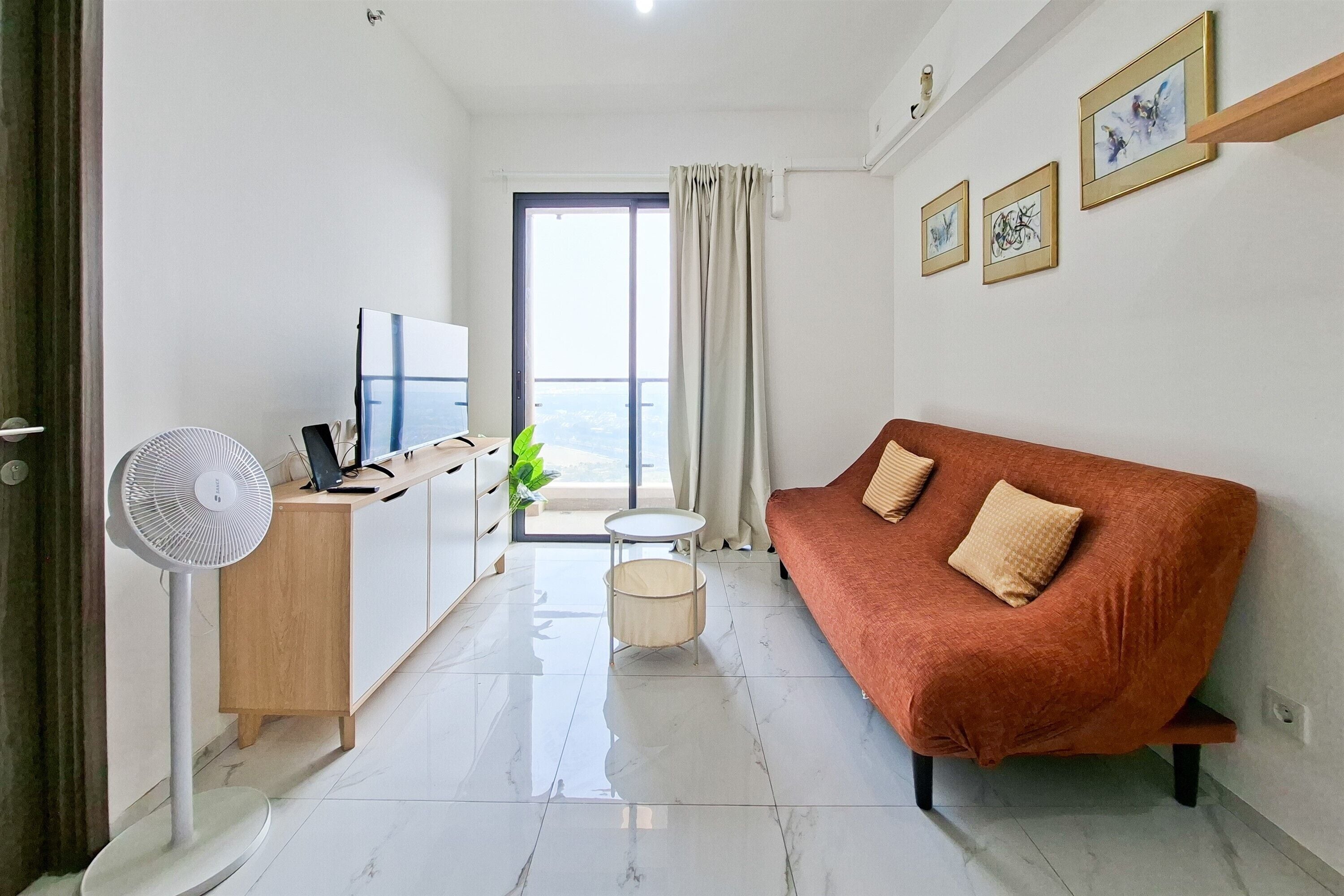 A modern living room with a sofa, a TV, a fan, and a balcony with a view.