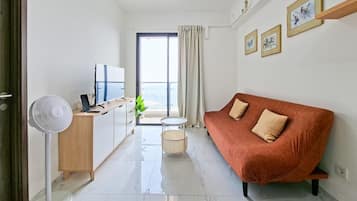 A modern living room with a sofa, a TV, a fan, and a balcony with a view.