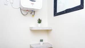 A bathroom with a white wall, a white heater, and two shelves with potted plants. - Best Deal Studio At Apartment Meikarta District 2 (Cikarang)