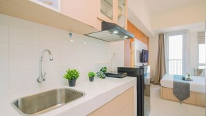 A modern kitchen with a stainless steel sink, a built-in stove, and a flat-screen TV mounted on the wall. - Warm Studio Room With City View At Apartment Tokyo Riverside Pik 2 (Teluknaga)