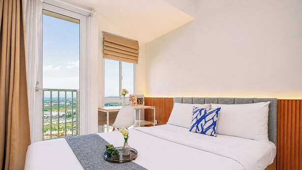 A hotel room with a bed, a desk, a chair, and a view of the city. - Warm Studio Room With City View At Apartment Tokyo Riverside Pik 2 (Teluknaga)