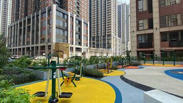 Un parque infantil con equipamiento de ejercicio rodeado de vegetación y edificios al fondo.