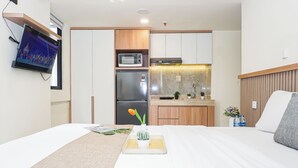 Una camera d'albergo con un letto, un angolo cottura, una TV a parete e una finestra.