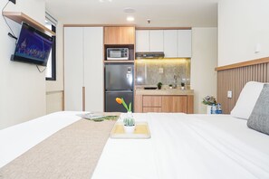 Ein Hotelzimmer mit Bett, einer kleinen Küchenzeile, einem an der Wand befestigten Fernseher und einem Fenster.