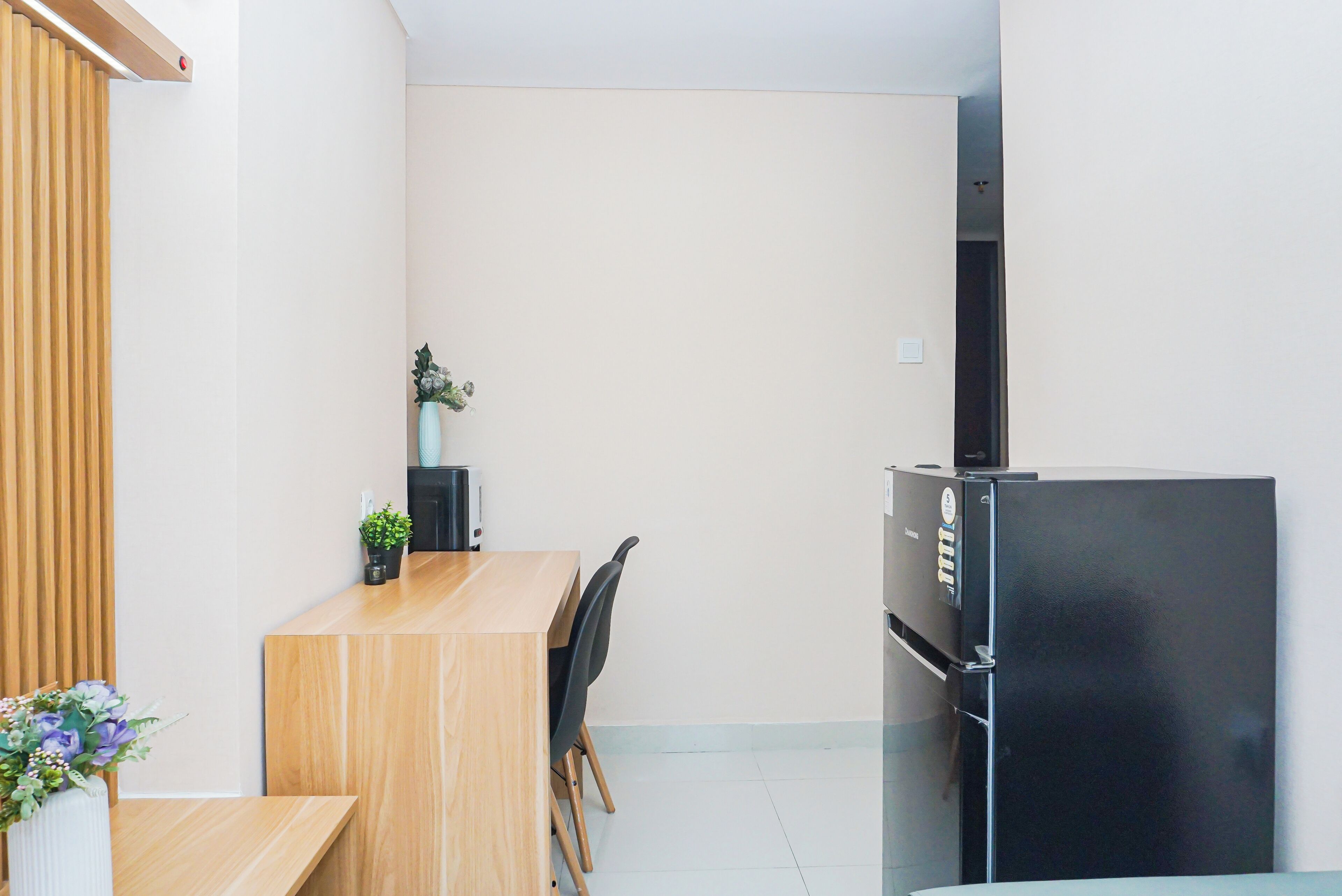 A compact kitchen with a wooden table, chairs, a black refrigerator, and a potted plant.