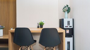 A room with a wooden desk, two black chairs, a small potted plant, a water dispenser, and a whiteboard. - Modern Look 2Br Apartment Pollux Chadstone (Cikarang)