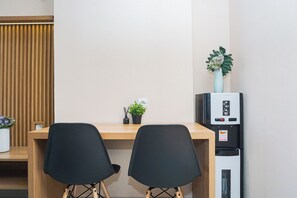 A room with a wooden desk, two black chairs, a small potted plant, a water dispenser, and a whiteboard. - Modern Look 2Br Apartment Pollux Chadstone (Cikarang)