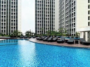 A swimming pool with lounge chairs and tall buildings in the background. - Modern Look 2Br Apartment Pollux Chadstone (Cikarang)