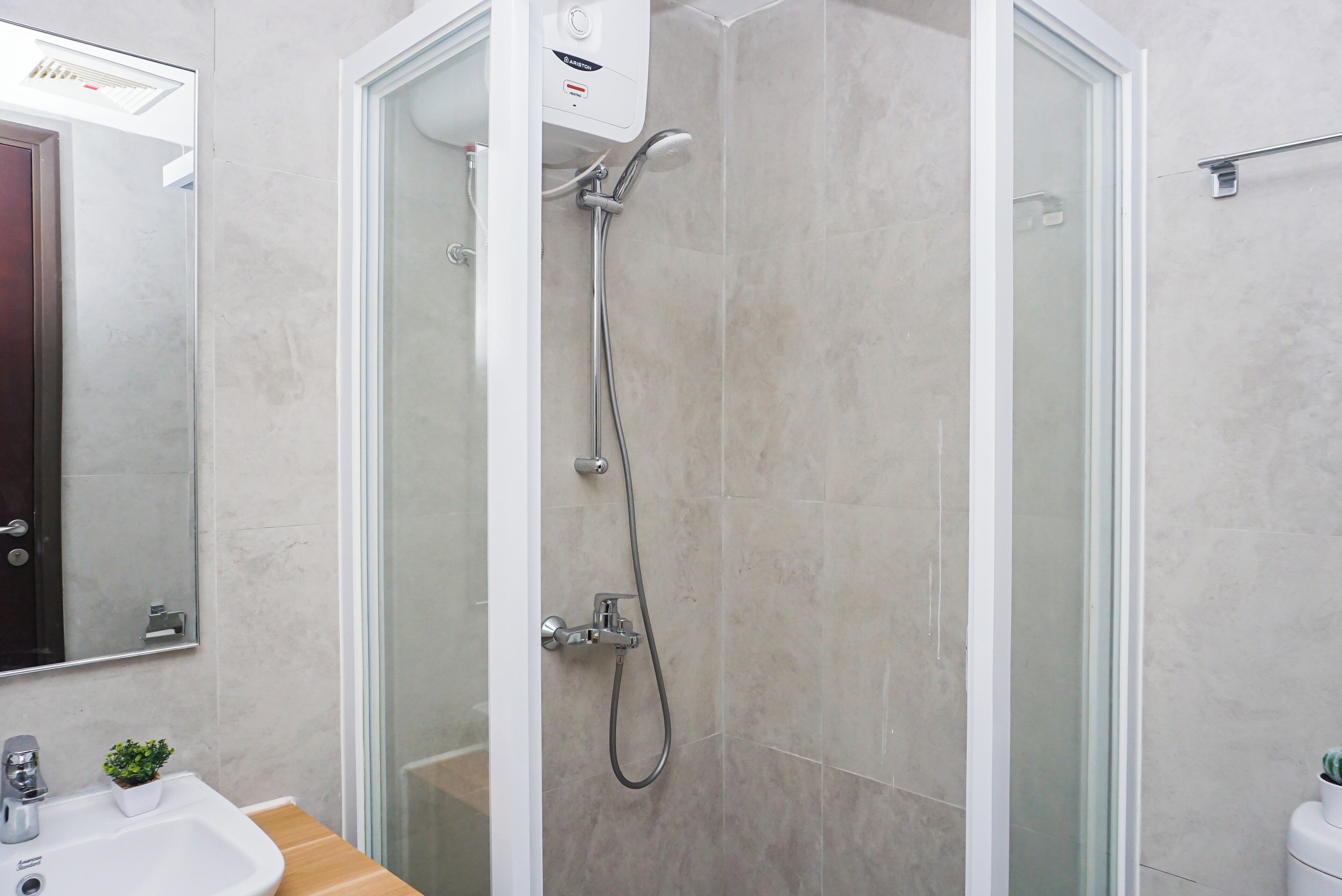 A modern bathroom with a glass shower enclosure, a white sink, and a potted plant.