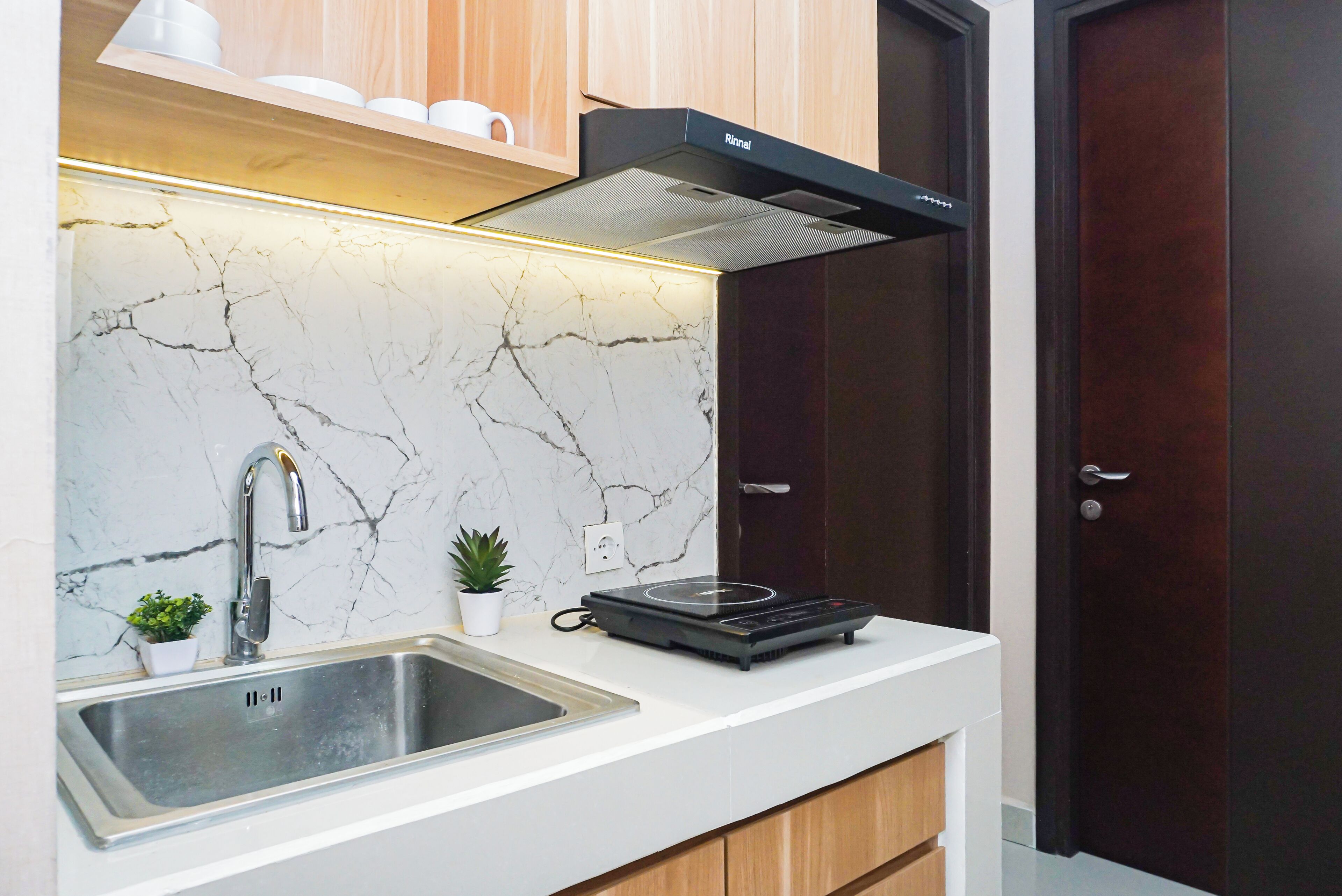 A modern kitchen with a marble backsplash, stainless steel sink, and a black range hood.