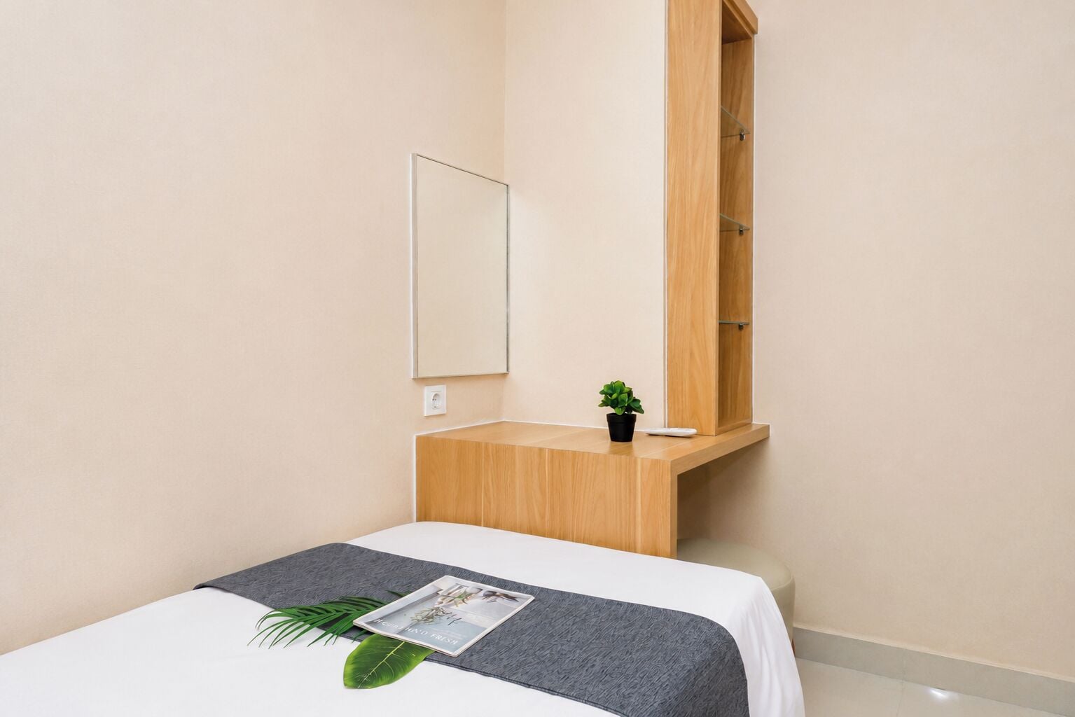 Quarto de hotel com uma cama, mesinha de madeira, espelho e planta em vaso.