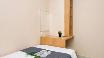 Quarto de hotel com uma cama, mesinha de madeira, espelho e planta em vaso.