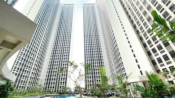 A modern high-rise building with a swimming pool surrounded by greenery.