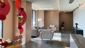 Um lobby de hotel moderno com balcão de recepção, sofás e uma parede decorativa com ventiladores e flores.