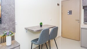 Quarto pequeno e moderno com parede de mármore, porta de madeira, uma pequena mesa com uma planta em vaso e duas cadeiras cinzentas.