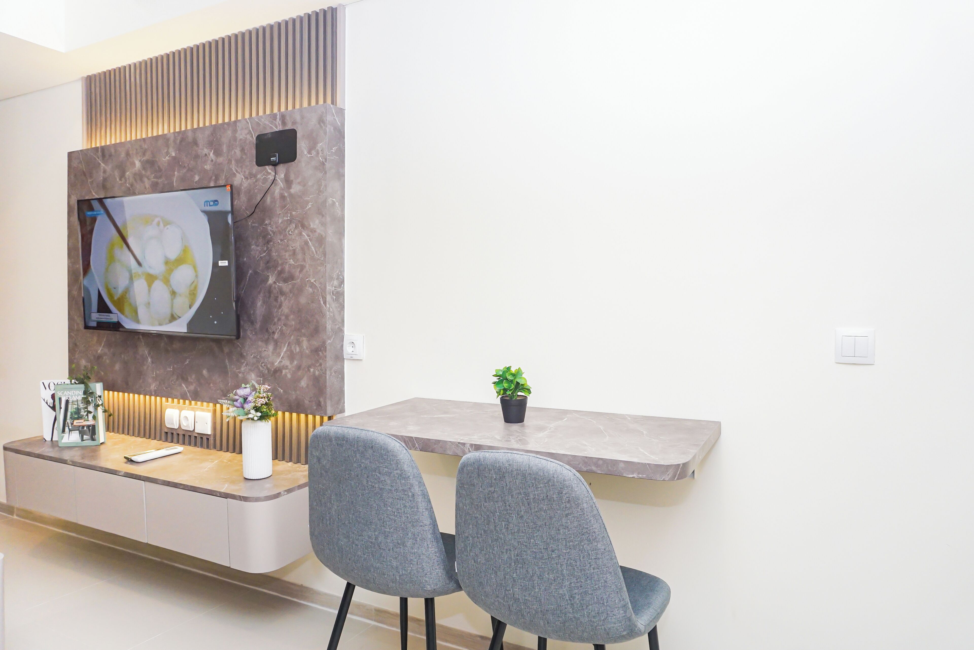 A modern kitchen with a built-in TV, a marble countertop, and two grey chairs.