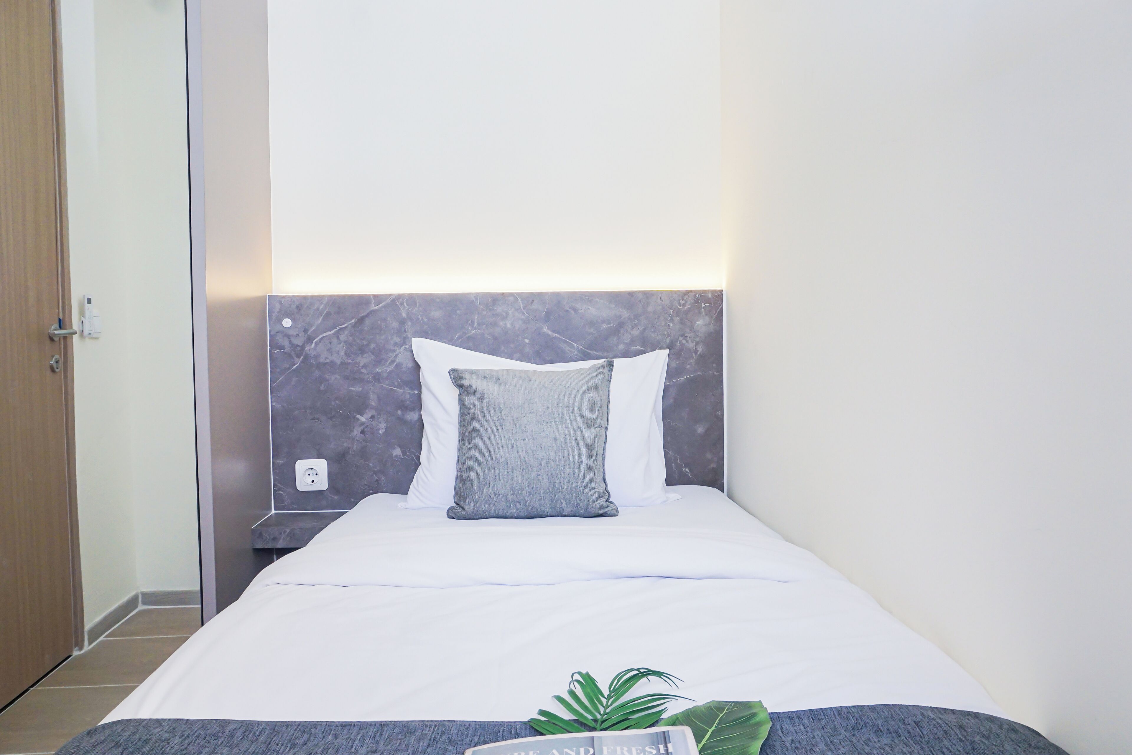 A hotel room with a bed, a nightstand, a wall socket, and a door.