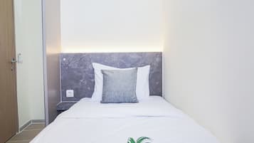 A hotel room with a bed, a nightstand, a wall socket, and a door.