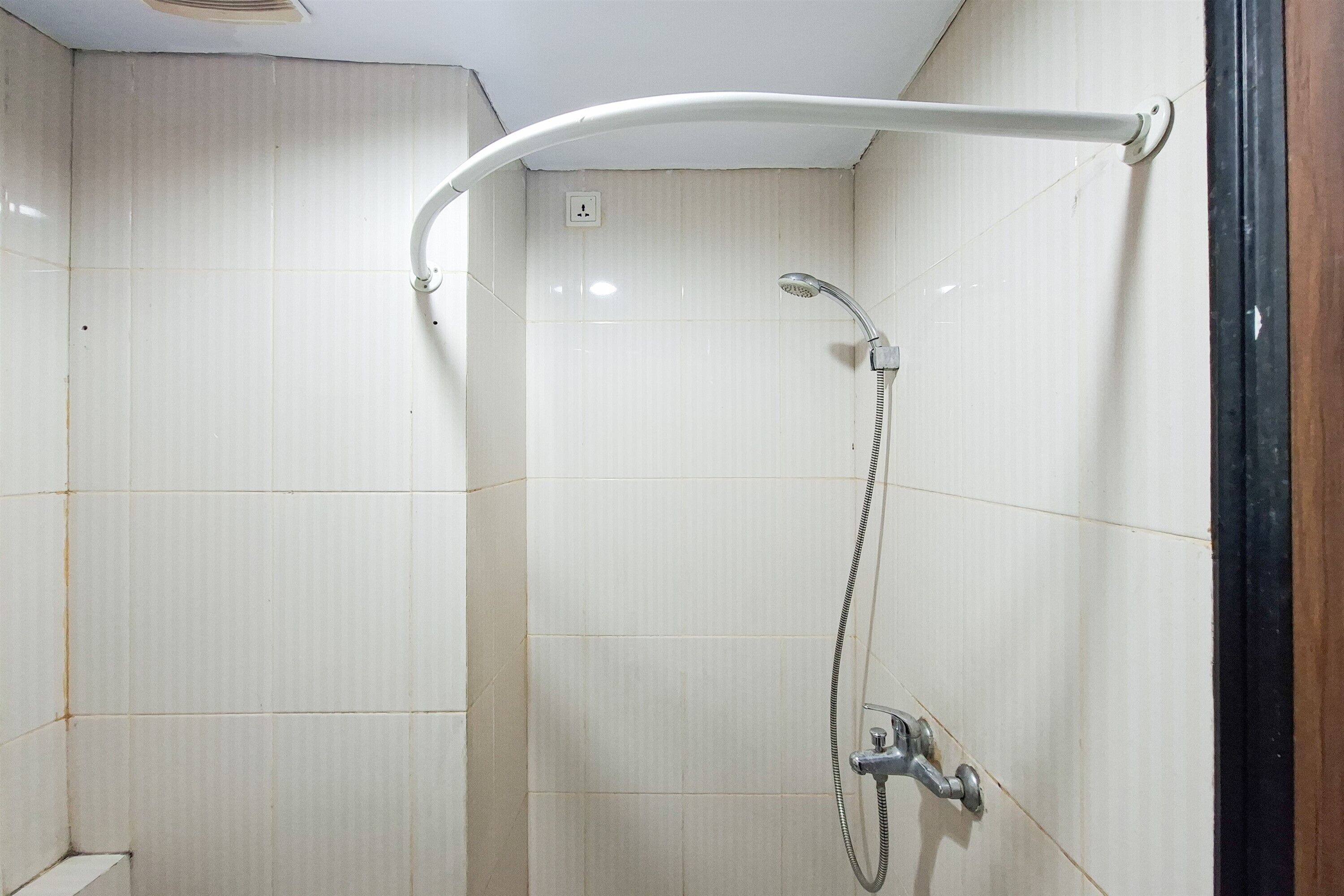 Une douche équipée d’un pommeau de douche à main et d’un pommeau de douche fixe, tous deux fixés sur un mur recouvert de carreaux blancs.