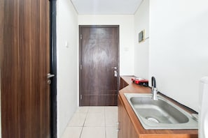 Passadís petit i estret amb una porta de fusta, un paviment de rajoles i una zona de cuina amb un rentaplats i un electrodomèstic vermell.