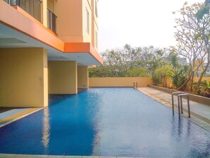 A swimming pool with a metal ladder, surrounded by a low wall and plants. - Elegant & Cozy Living 2Br Boutique Kemayoran Apartment Next To Citra Xperience Mall (Jakarta)