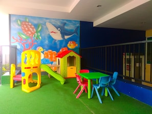 A children's play area with colorful play structures, a mural, and a seating area with chairs and a table. - Elegant & Cozy Living 2Br Boutique Kemayoran Apartment Next To Citra Xperience Mall (Jakarta)