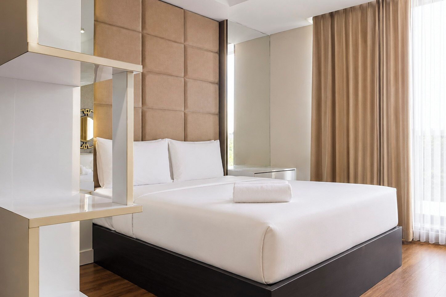 Ein modernes Hotelzimmer mit einem großen Bett, einem Nachttisch, einem Spiegel und Blick ins Freie.