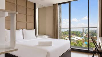 Une chambre d’hôtel avec un grand lit, une table de chevet, une chaise et une vue sur le paysage urbain grâce à de grandes fenêtres.
