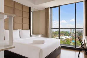 Une chambre d’hôtel avec un grand lit, une table de chevet, une chaise et une vue sur le paysage urbain grâce à de grandes fenêtres.