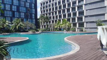 Une piscine dotée d’une terrasse en bois, entourée de palmiers et de bâtiments modernes.