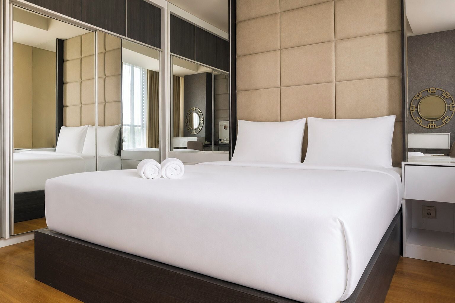 Une chambre d’hôtel avec un grand lit, une table de chevet, un miroir et une horloge murale.