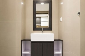 Une salle de bain moderne avec un lavabo blanc, des meubles de rangement aux couleurs foncées et un miroir au-dessus du lavabo.