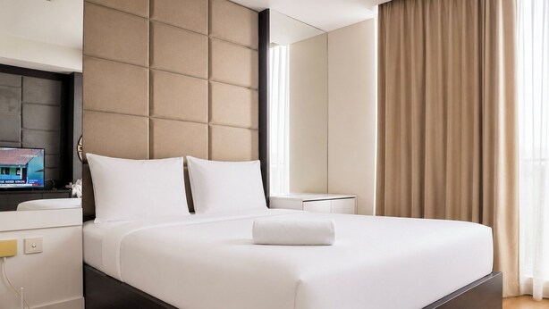 A modern hotel room with a large bed, a flat-screen TV, a bedside table, and a window with curtains.
