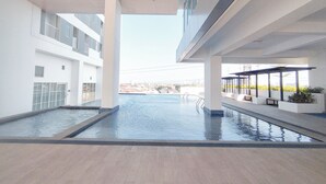 A modern indoor swimming pool with clear water, surrounded by white walls and a view of a cityscape. - Modern And Convenient Studio At Apartment Kyo Society (Surabaya)