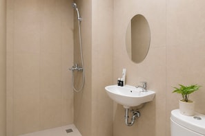 Et badeværelse med bruser, vask, spejl og toilet.