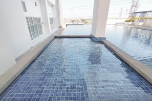 En swimmingpool med flisegulv og udsigt til boligområde i baggrunden.