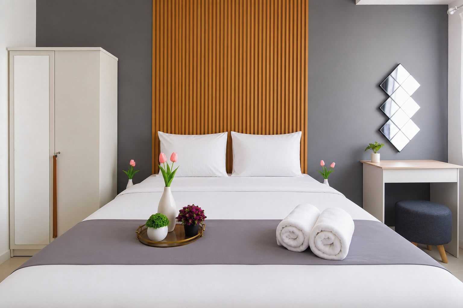 A modern hotel room with a bed, bedside table, and a desk with a chair.