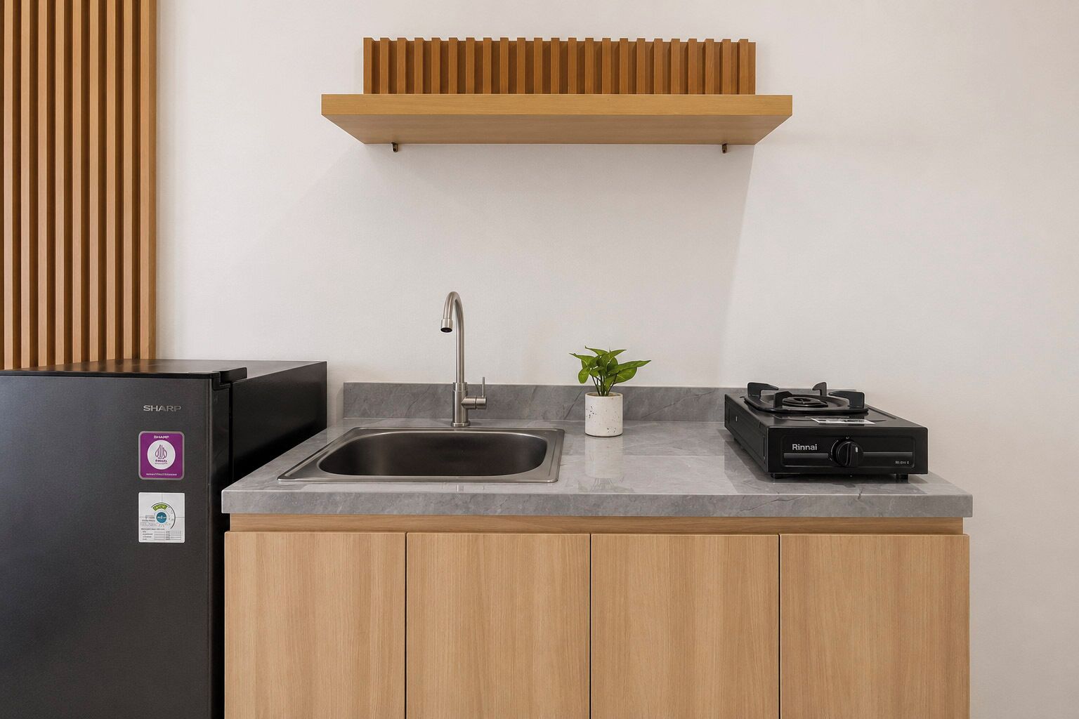 A kitchen with a built-in sink, a black refrigerator, a stove, and a small potted plant.