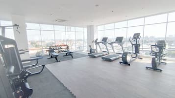 A gym with cardio machines, weight equipment, and a view of the city through large windows.