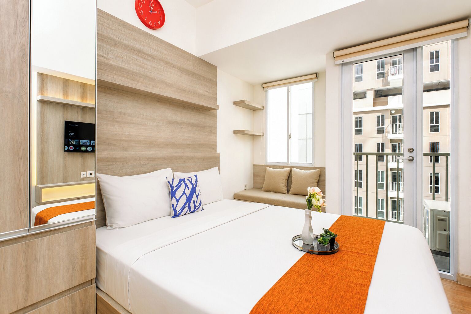 A modern hotel room with a bed, a TV, a sofa, and a balcony with a view of the city.