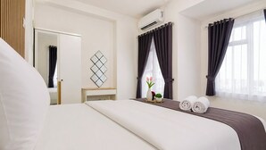 A hotel room with a bed, bedside table, air conditioning unit, window with curtains, and a wall-mounted decorative piece. - Warm And Stylish 1Br At Apartment Kyo Society (Surabaya)