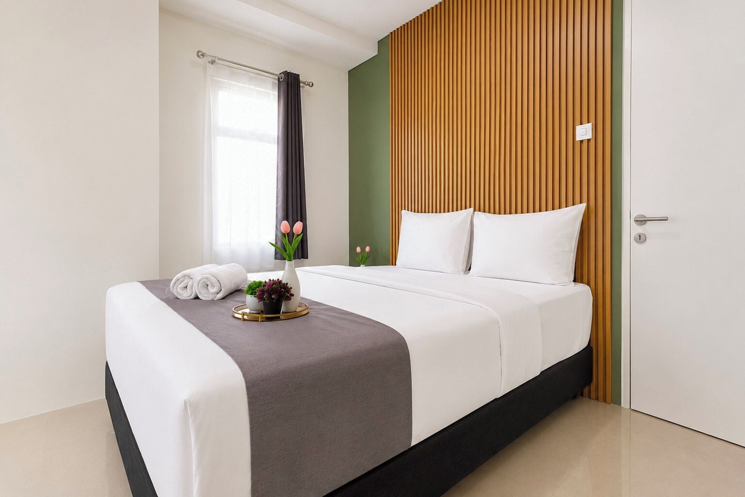 A neatly made bed with white linens, a grey throw, and a small vase with flowers.